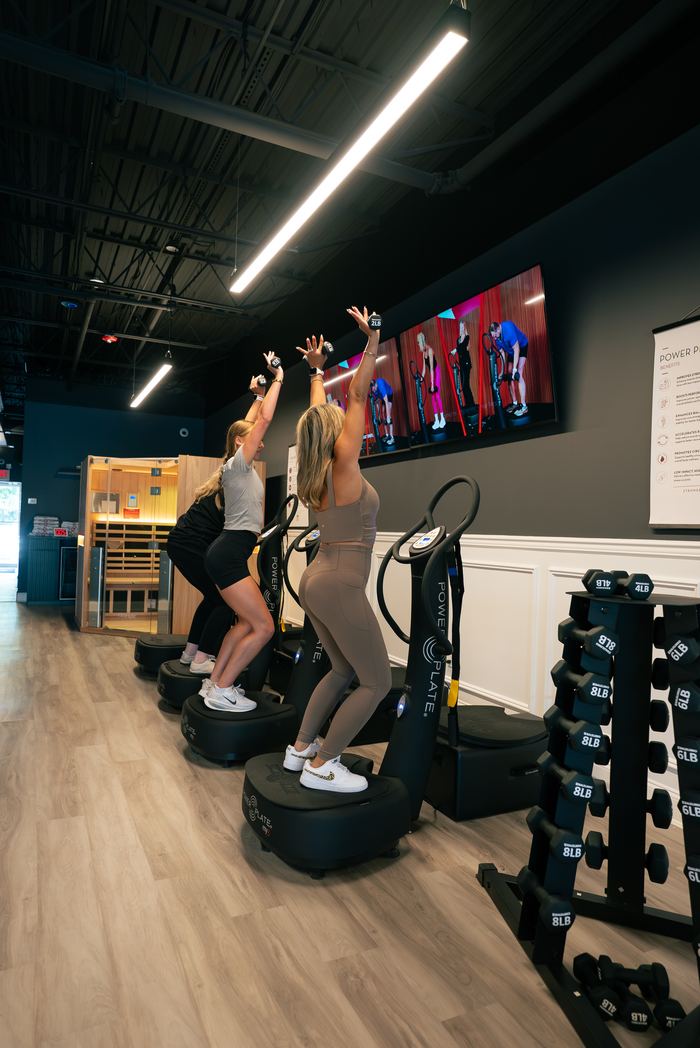 Two members reaching overhead on the Power Plate platforms during a class.