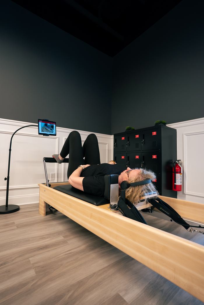 A member lying back on a Pilates reformer with the screen ready above.