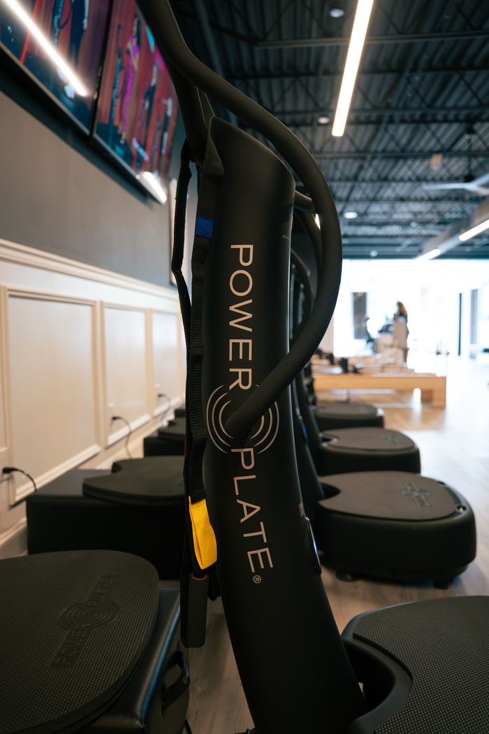 A row of Power Plate platforms with the class screens glowing behind them.